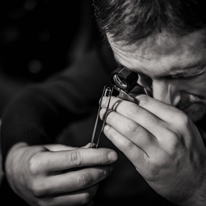 Image d'un homme regardant un composant électronique à la loupe, illustrant le savoir faire